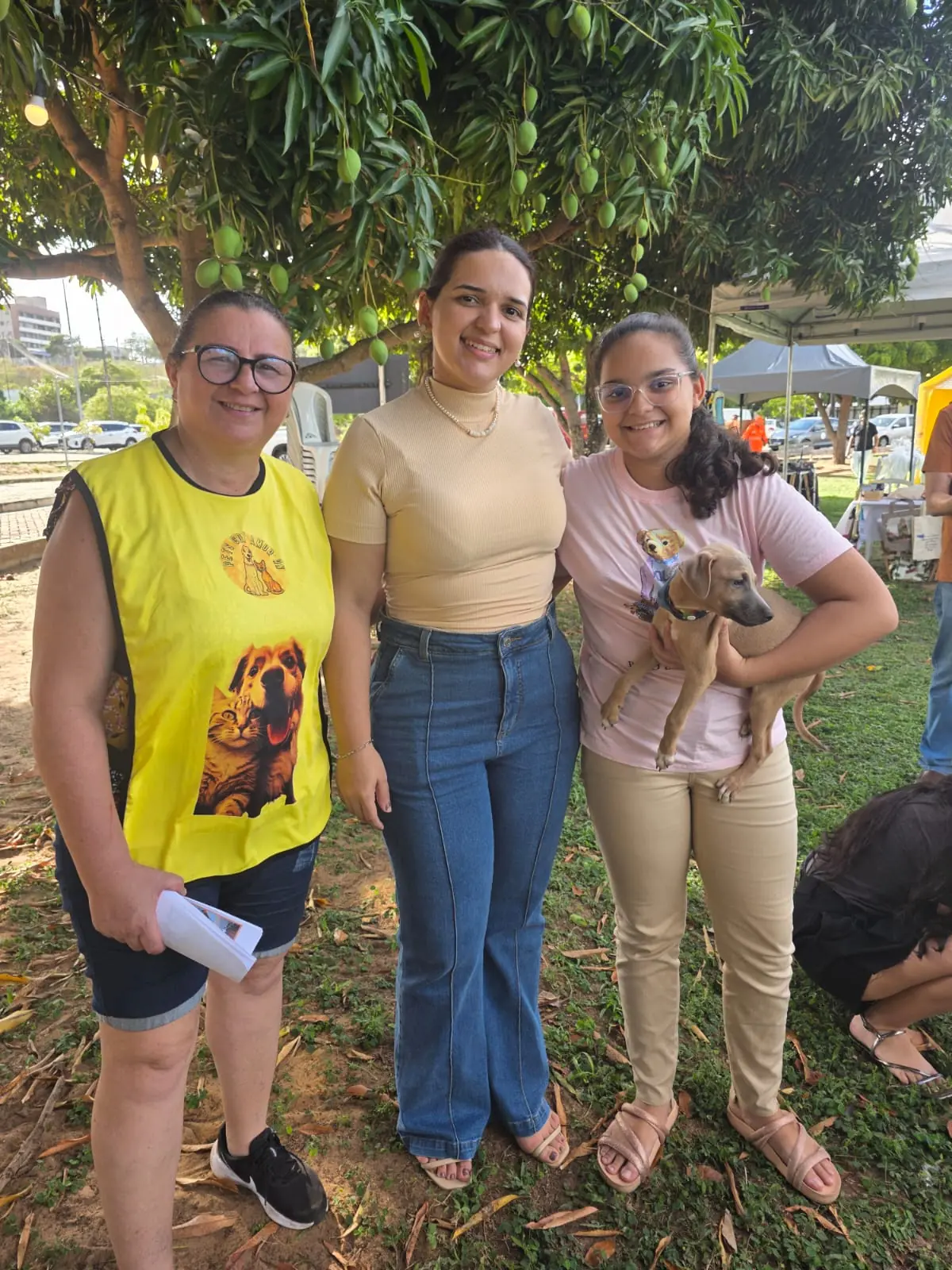 Voluntárias da ONG com um filhote nos braços sob uma mangueira